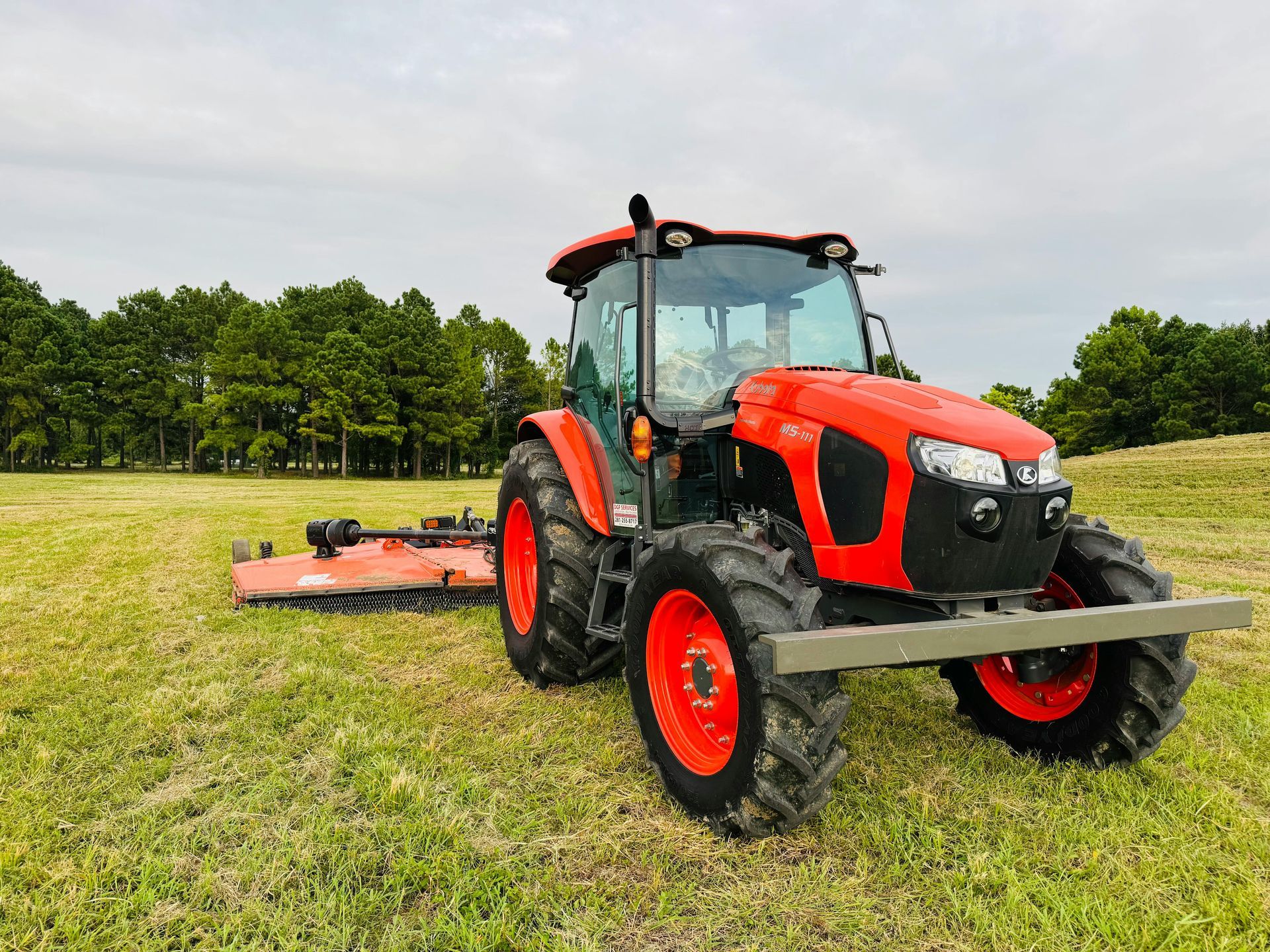 Red tractor with mower attachment in a grassy field.