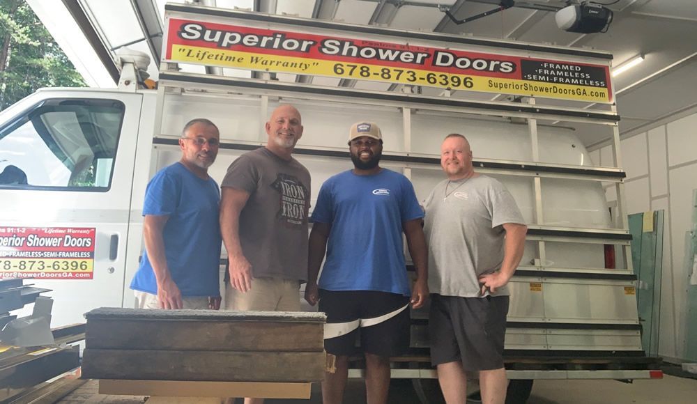 Four men are standing in front of a truck that says superior shower doors