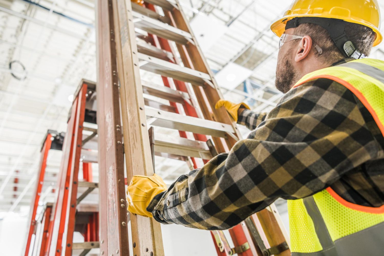 Construction worker climbing a ladder, wearing a hard hat, safety glasses, and high-visibility vest.