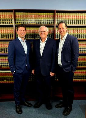 Three men in suits pose in front of a law library, smiling.