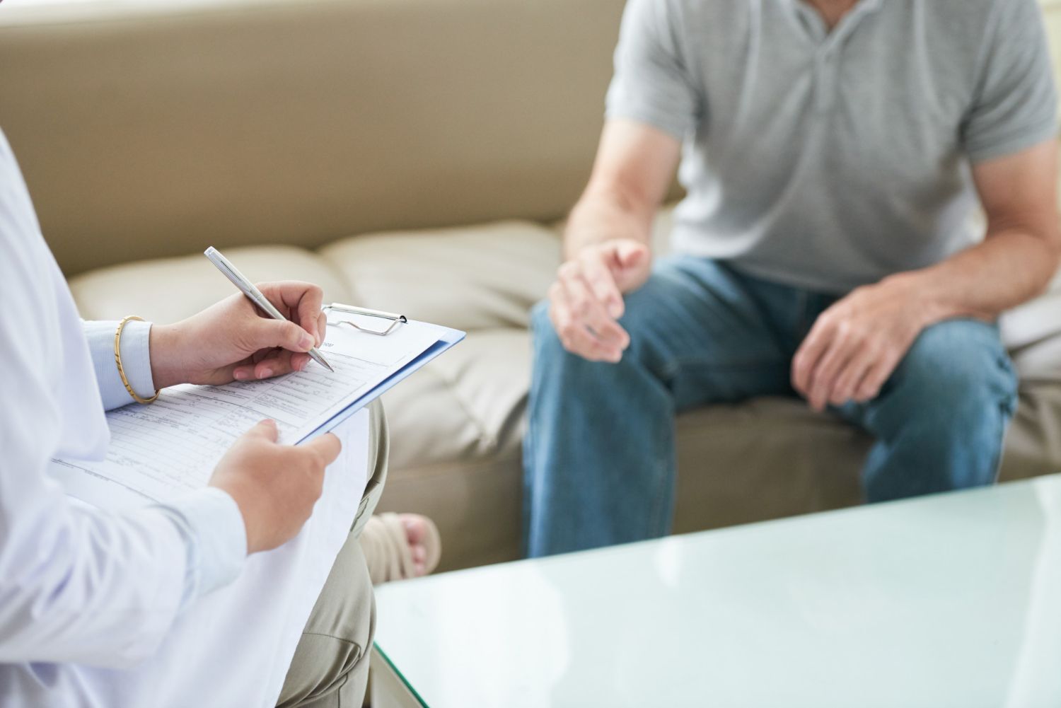 Doctor taking notes on a clipboard while interviewing a patient on a couch.