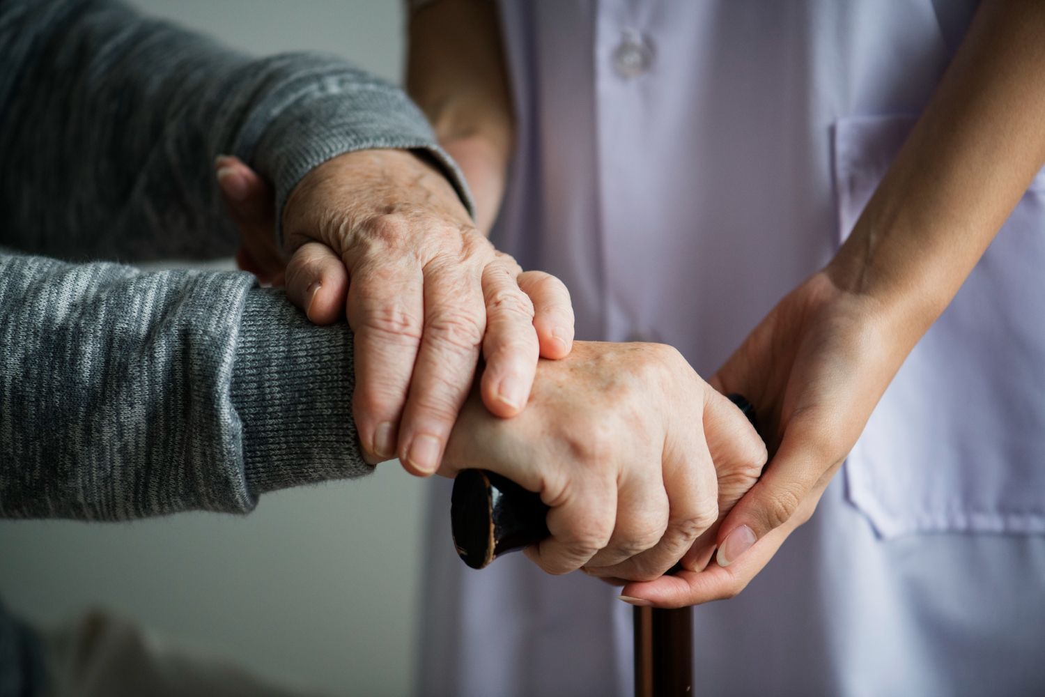 Hands of person holding cane being supported by another person.