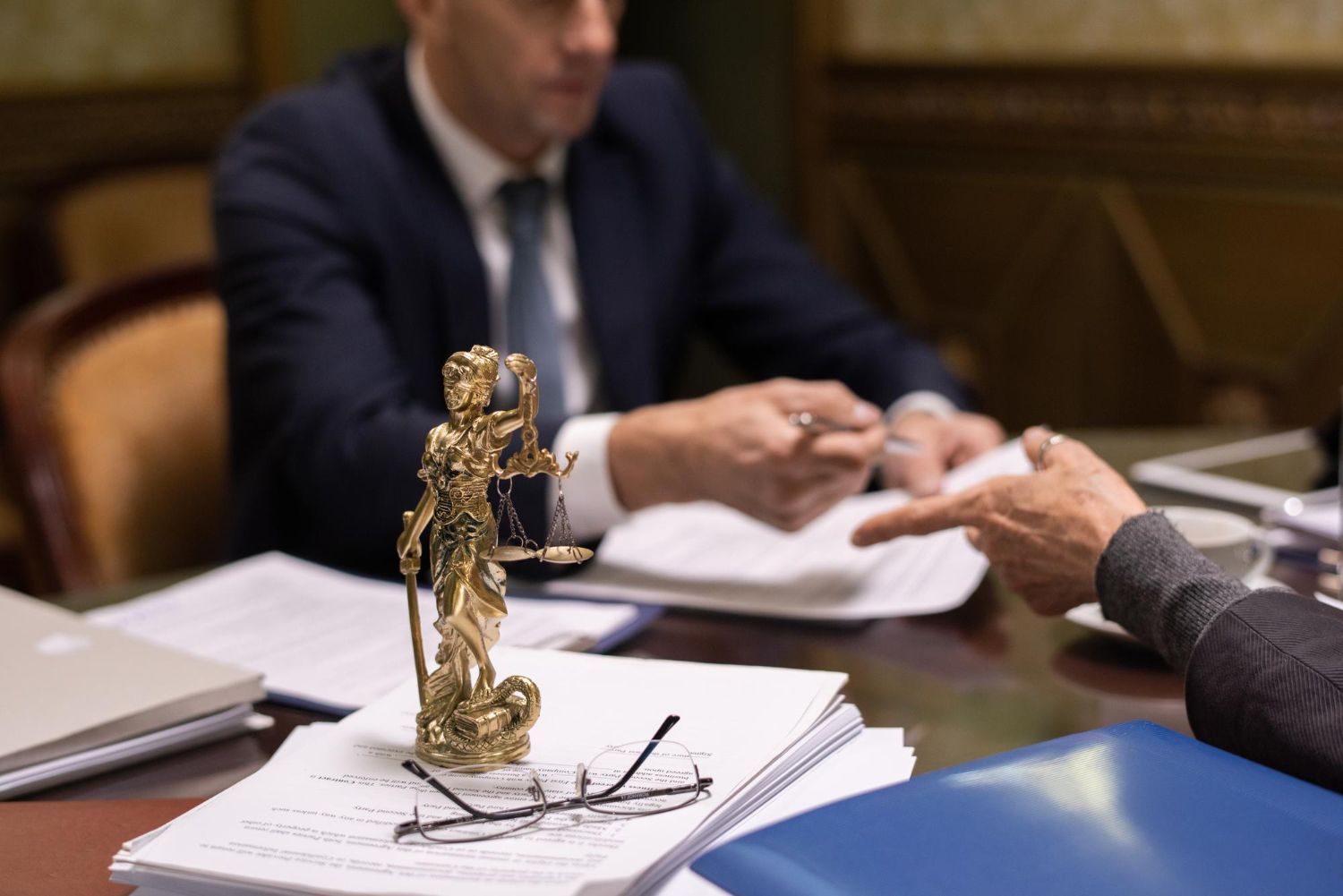 Statue of Lady Justice on paperwork in front of two people at a desk. One person points.