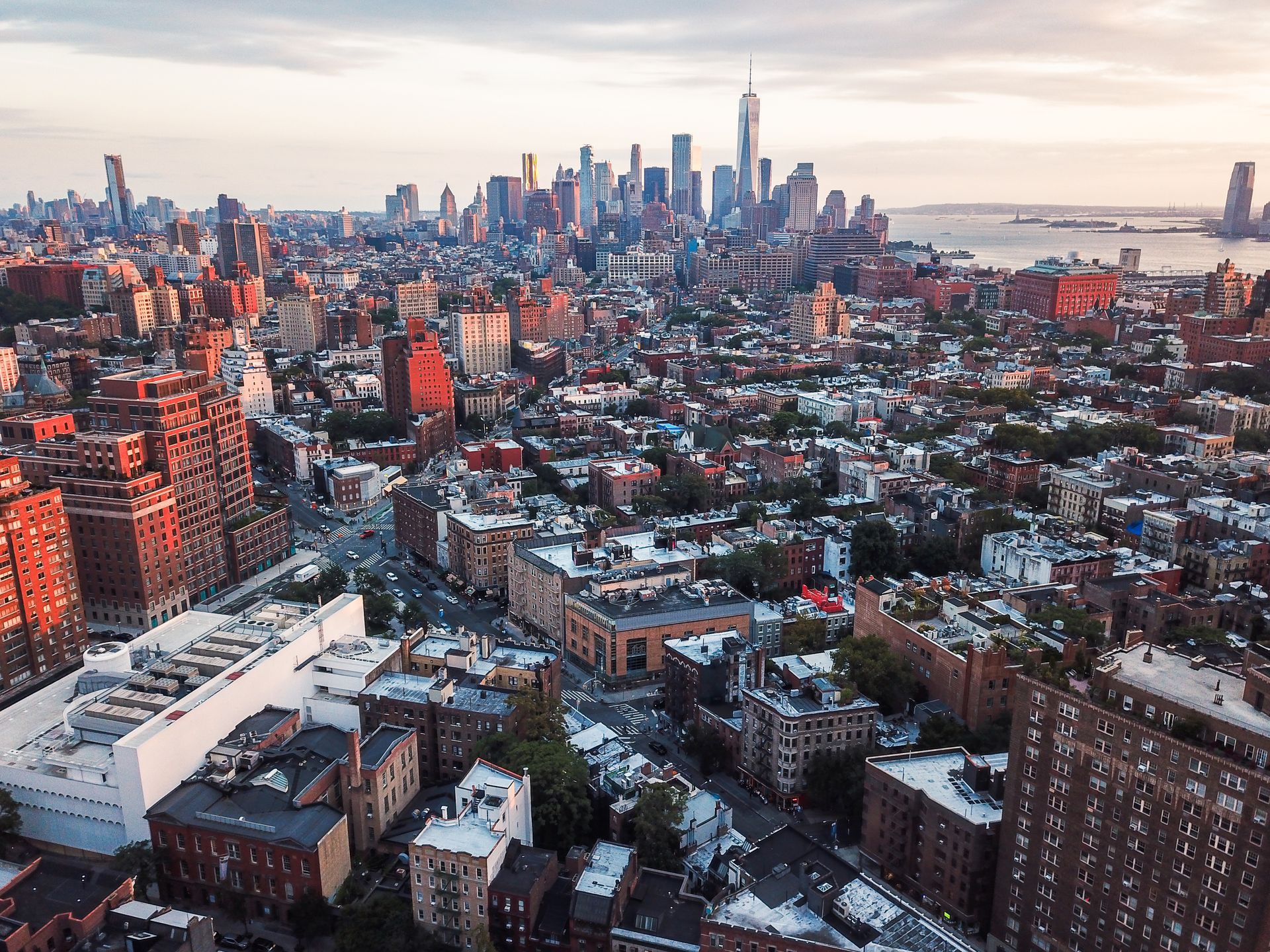 Aerial view of New York City buildings, with the World Trade Center in the distance at sunset.