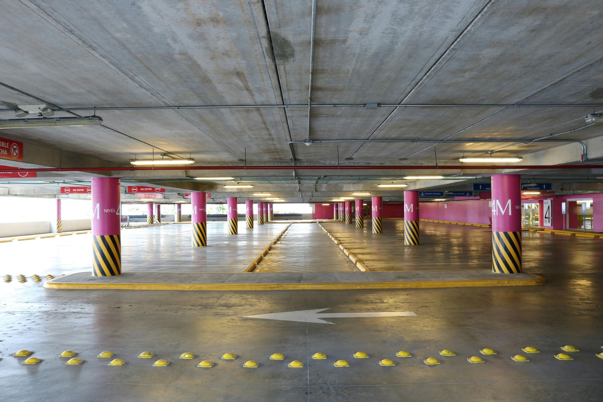 Empty parking garage with pink columns, yellow speed bumps, and overhead lighting.