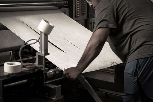 Person operating industrial machinery, inspecting a sheet of material.