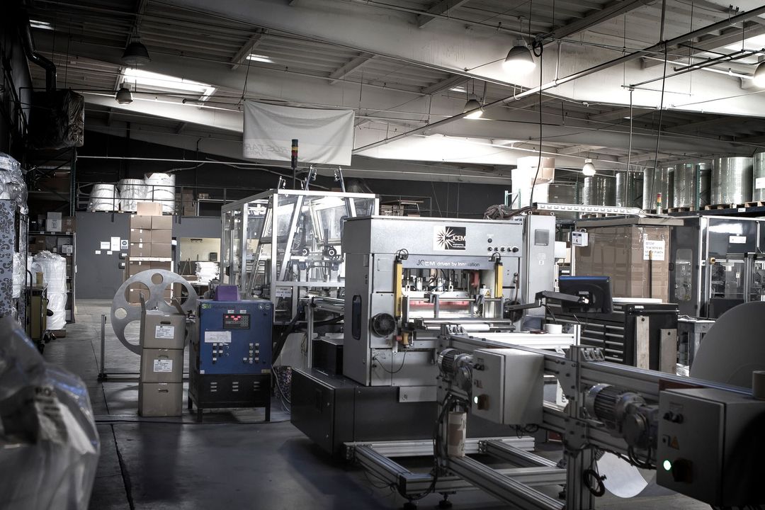 Industrial factory interior with machinery, boxes, and a worker in the background.