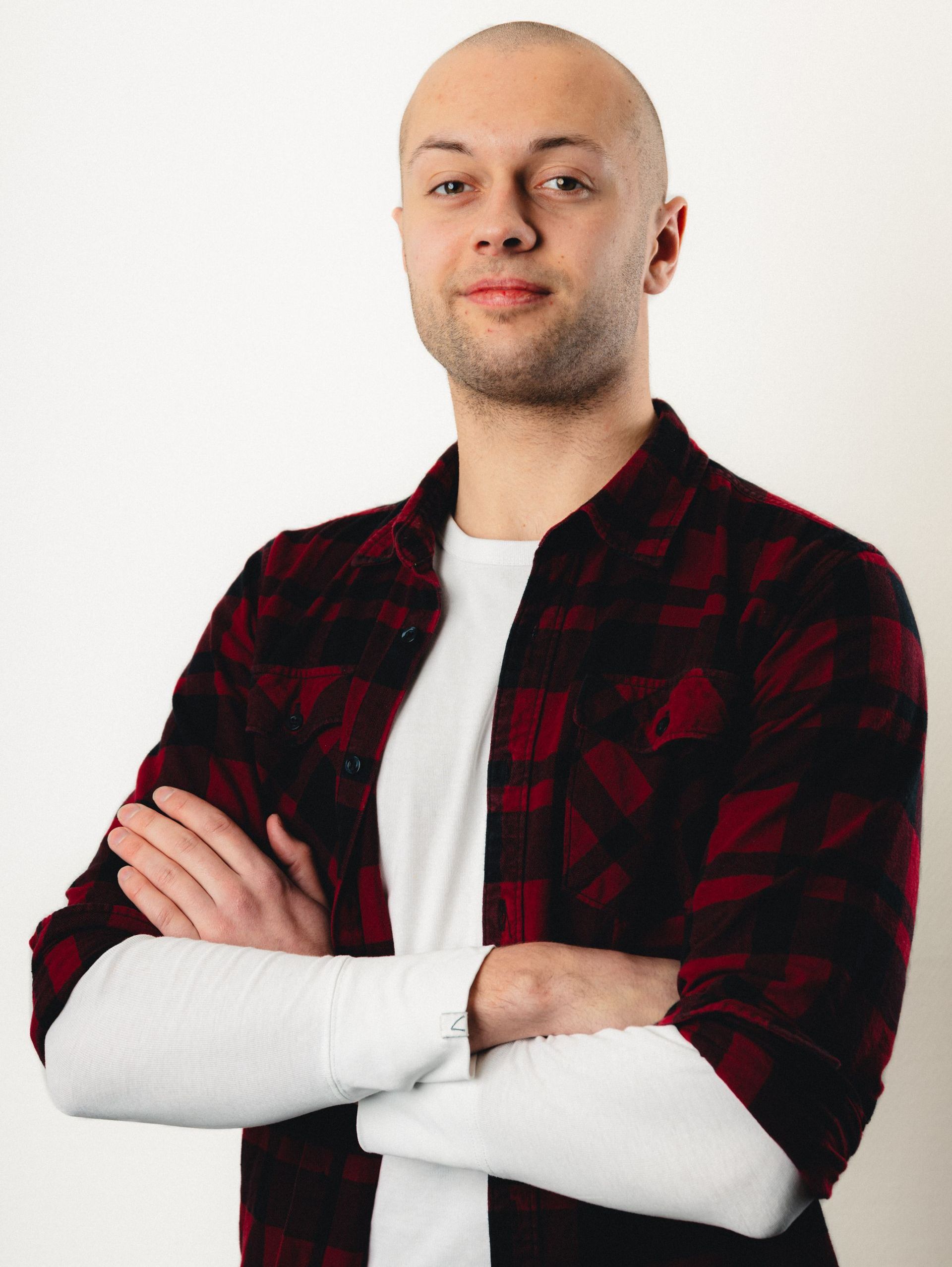 Een man in een geruit overhemd staat met zijn armen over elkaar.