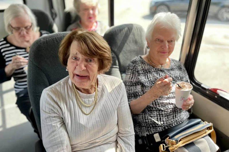 A group of older women are sitting on a bus eating ice cream.