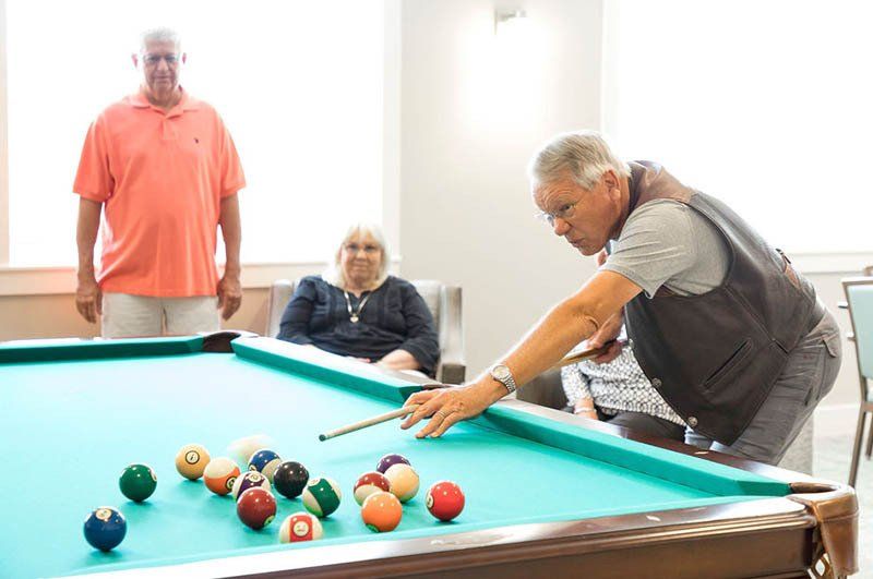 A man is playing pool in a room with other people.