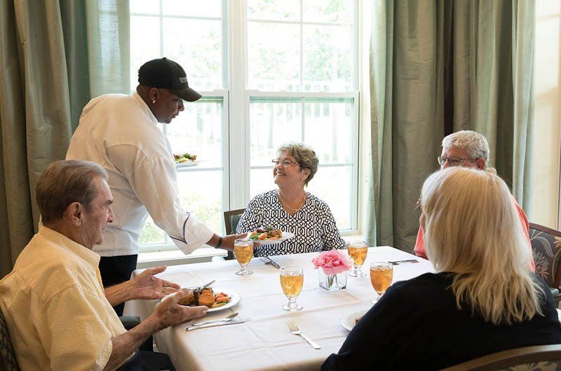 A man is serving food to a group of people sitting at a table.