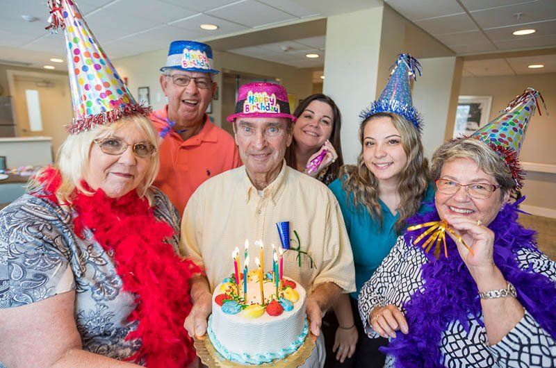 A group of people wearing party hats are standing around a birthday cake.