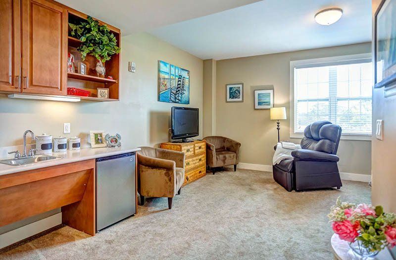 A living room with a television , chairs , a sink and a refrigerator.