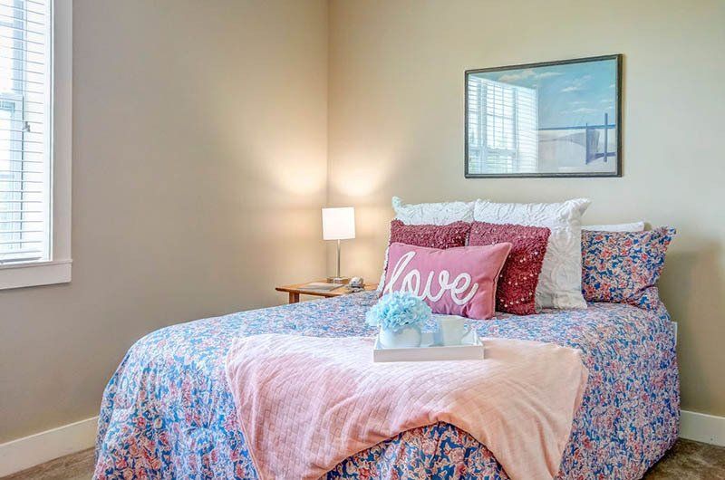 A bedroom with a bed , pillows , a lamp and a picture on the wall.