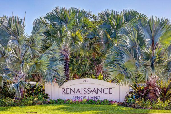 A sign for renaissance senior living is surrounded by palm trees.