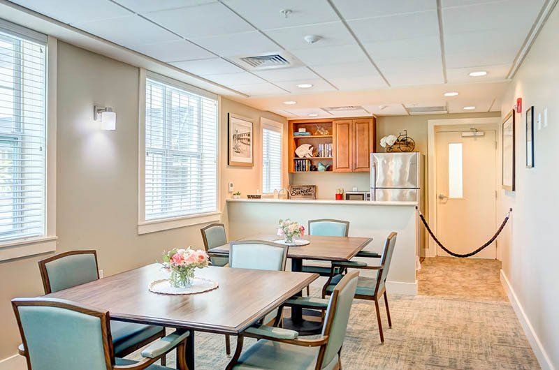 A dining room with tables and chairs and a kitchen in the background.