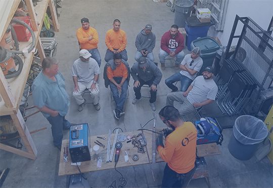 a group of men are sitting around a table in a workshop .
