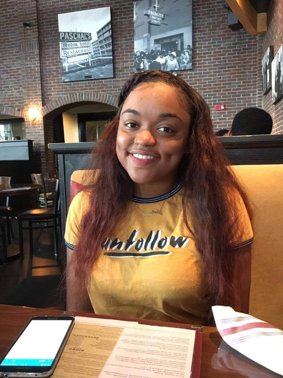 A woman in a yellow shirt is sitting at a table in a restaurant.