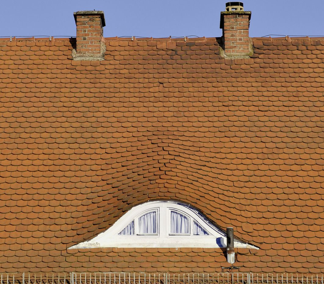 Red tiled roof with two brick chimneys, arched window, and small vent.