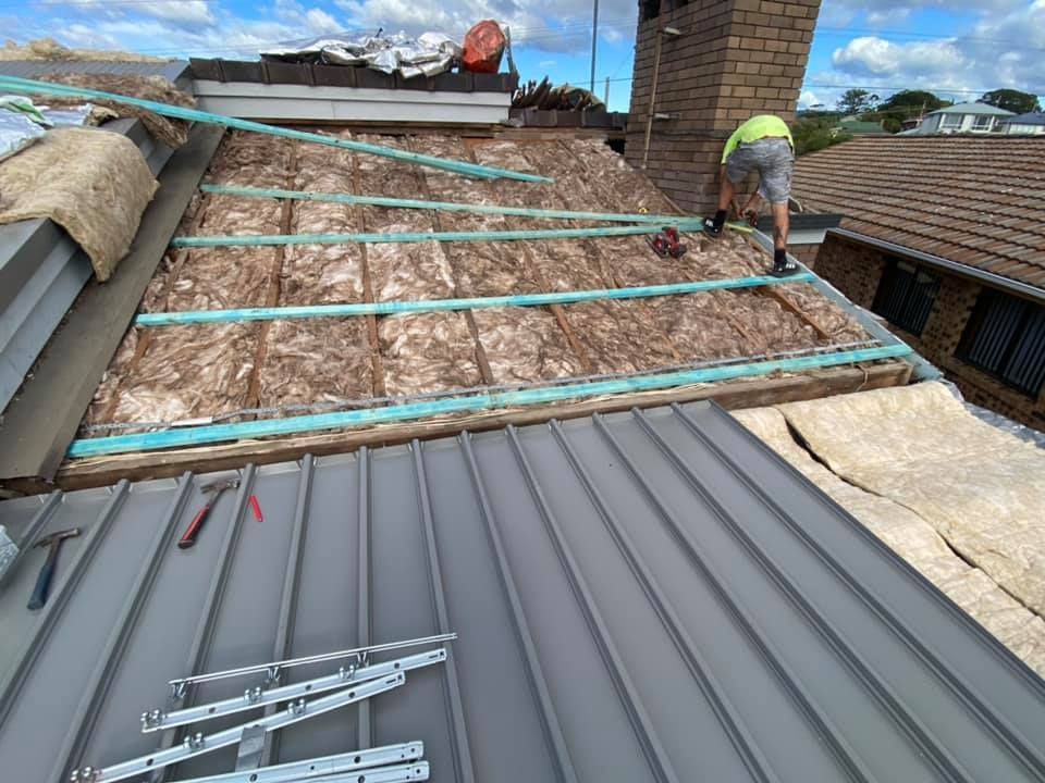 A Man Is Working On The Roof Of A House — Sattin's Metal Roofing In Avondale, NSW