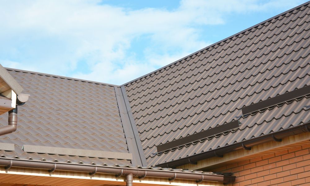 A Man Is Kneeling On Top Of A Roof Applying Sealant To It — Sattin's Metal Roofing In Avondale, NSW