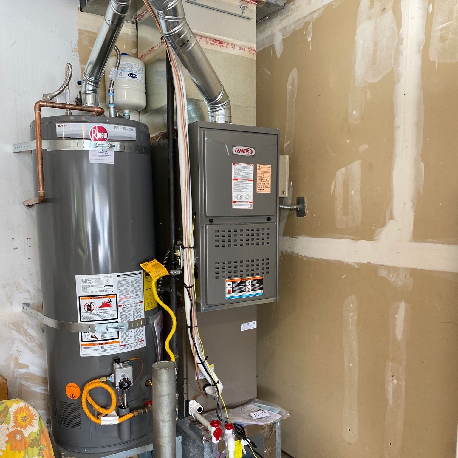 Water heater and furnace in a utility room with metal exhaust pipes and beige walls.