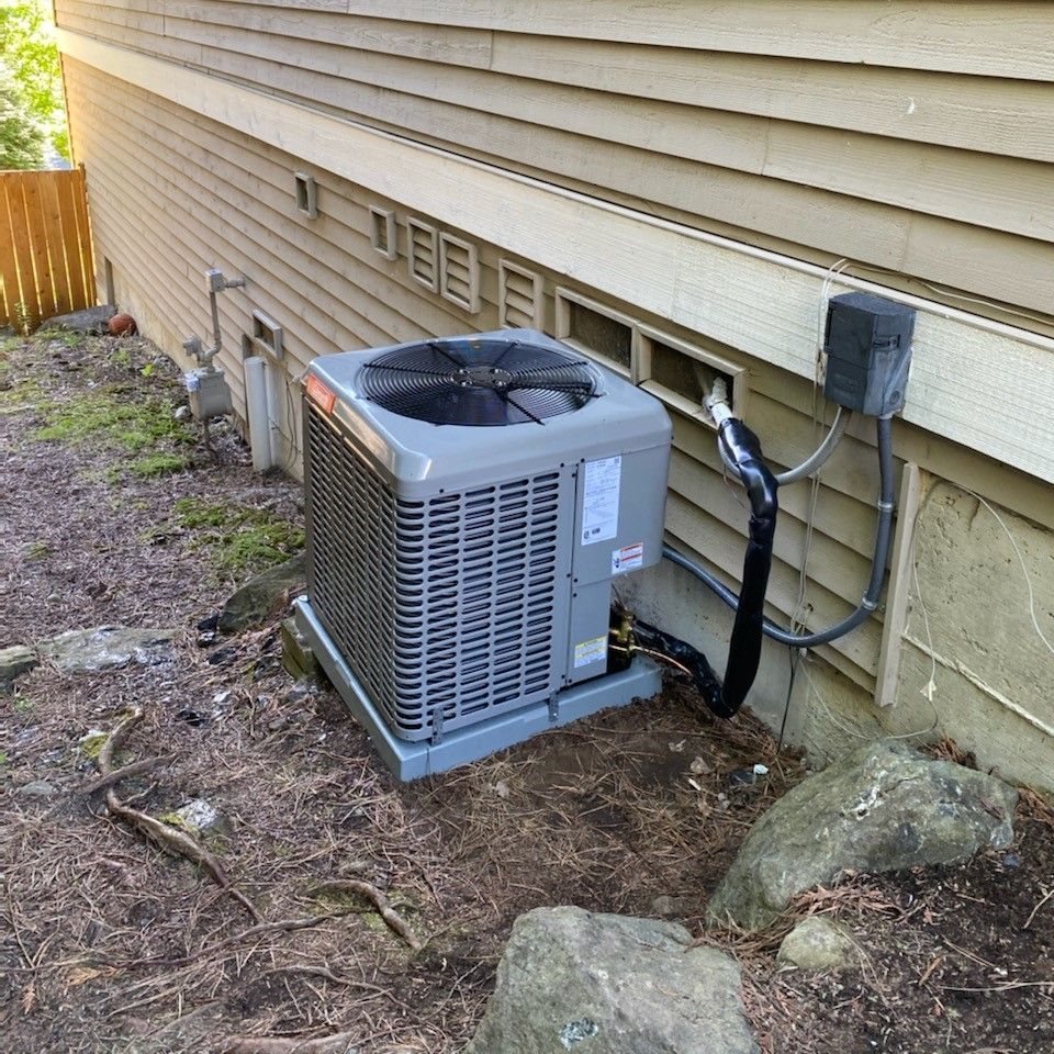 Air conditioning unit outside a building with beige siding, near rocks and foliage.