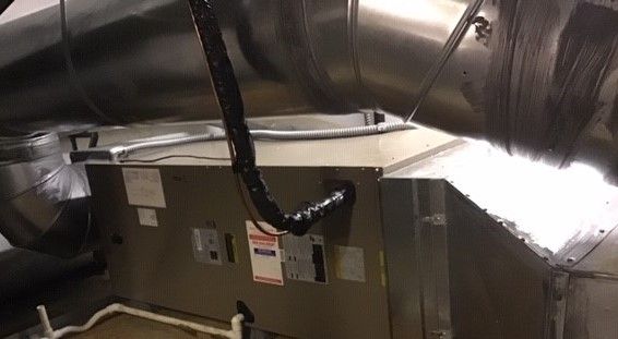 HVAC unit with ductwork in an indoor setting. Metal box, silver ducts, black insulated wire.