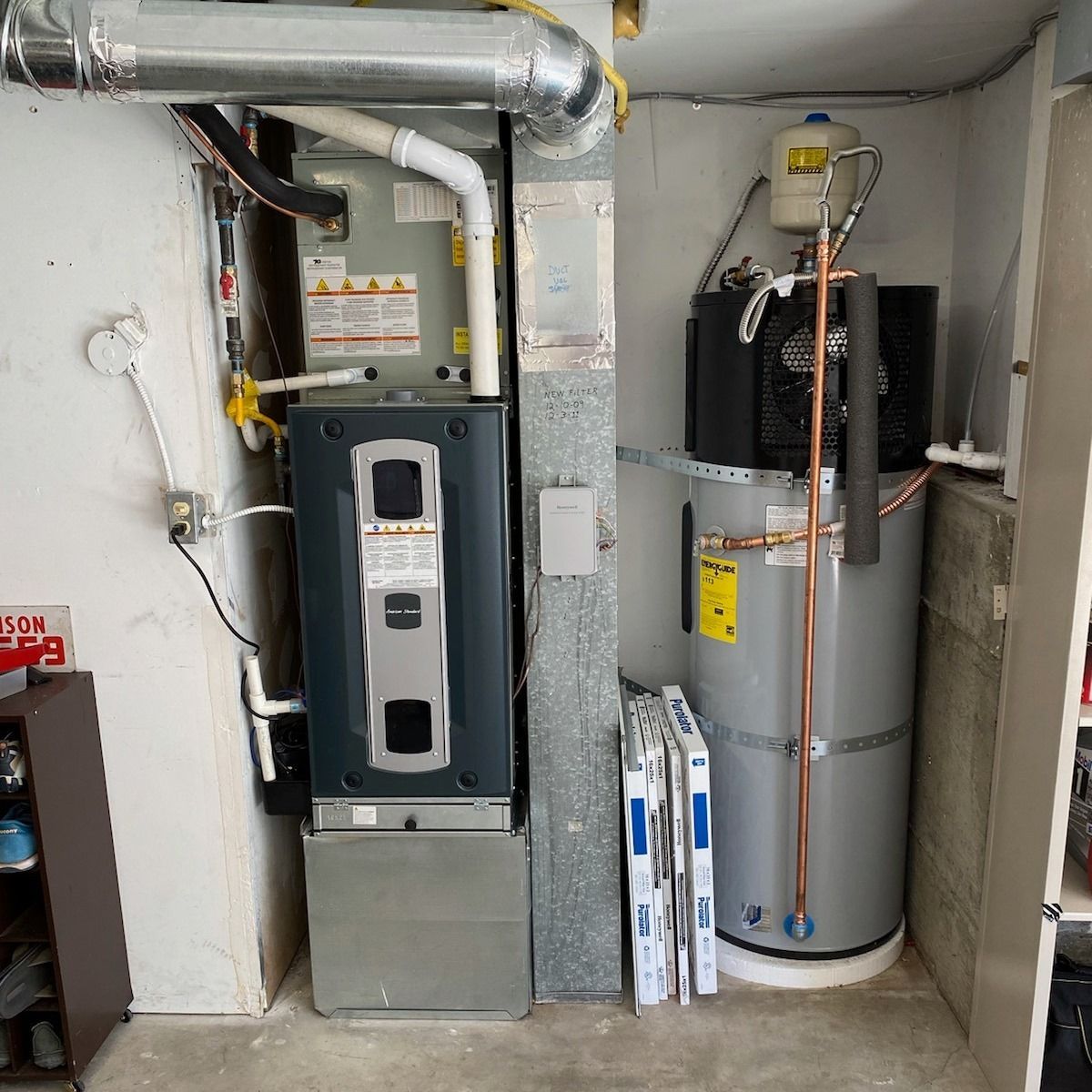 Furnace and water heater in a utility room. Gray and silver appliances stand against a white wall.