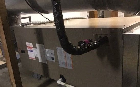 Furnace in a basement with flexible black ductwork connected to it.
