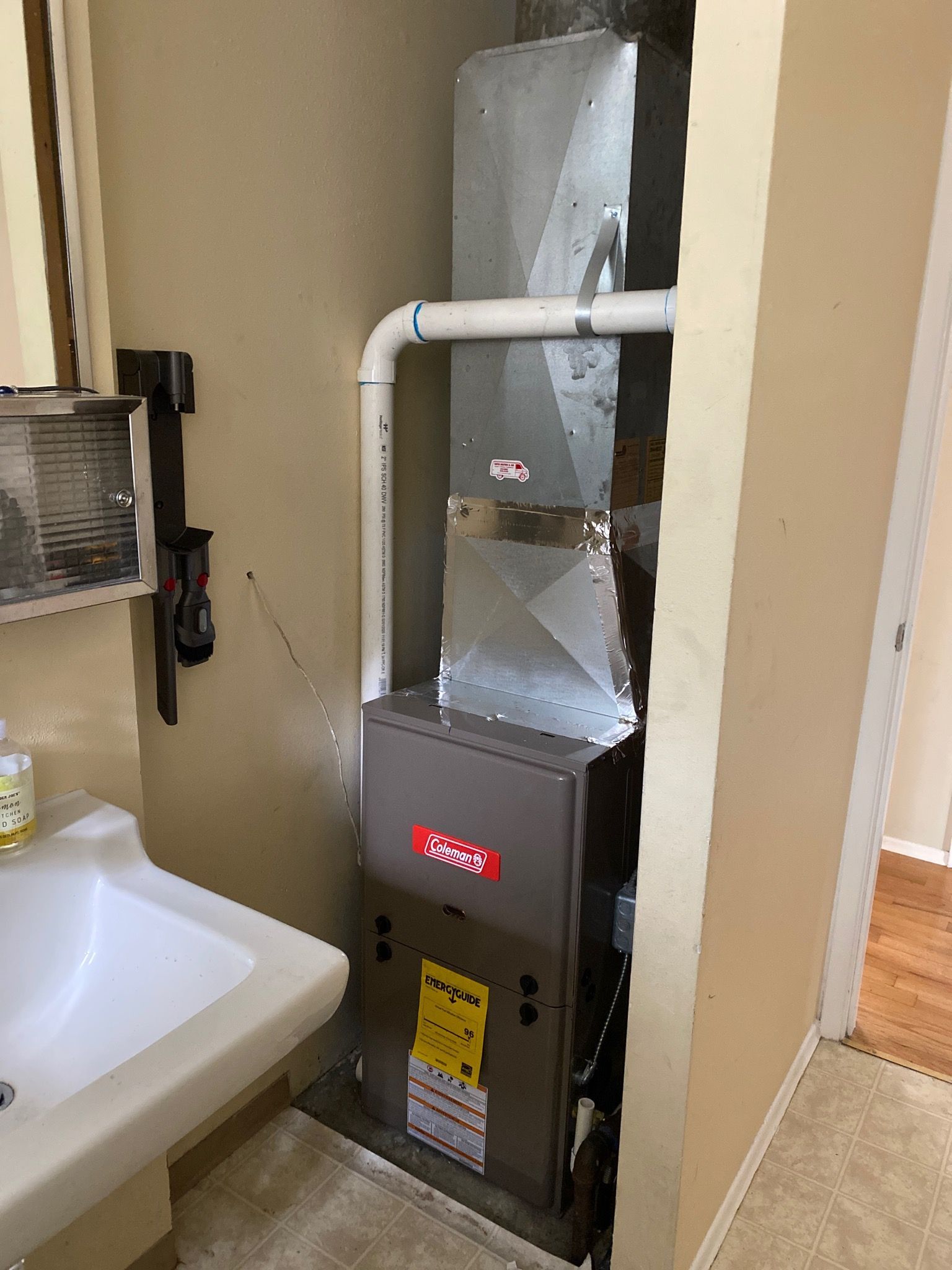 A furnace unit in a small bathroom, next to a sink, with a white vent pipe.