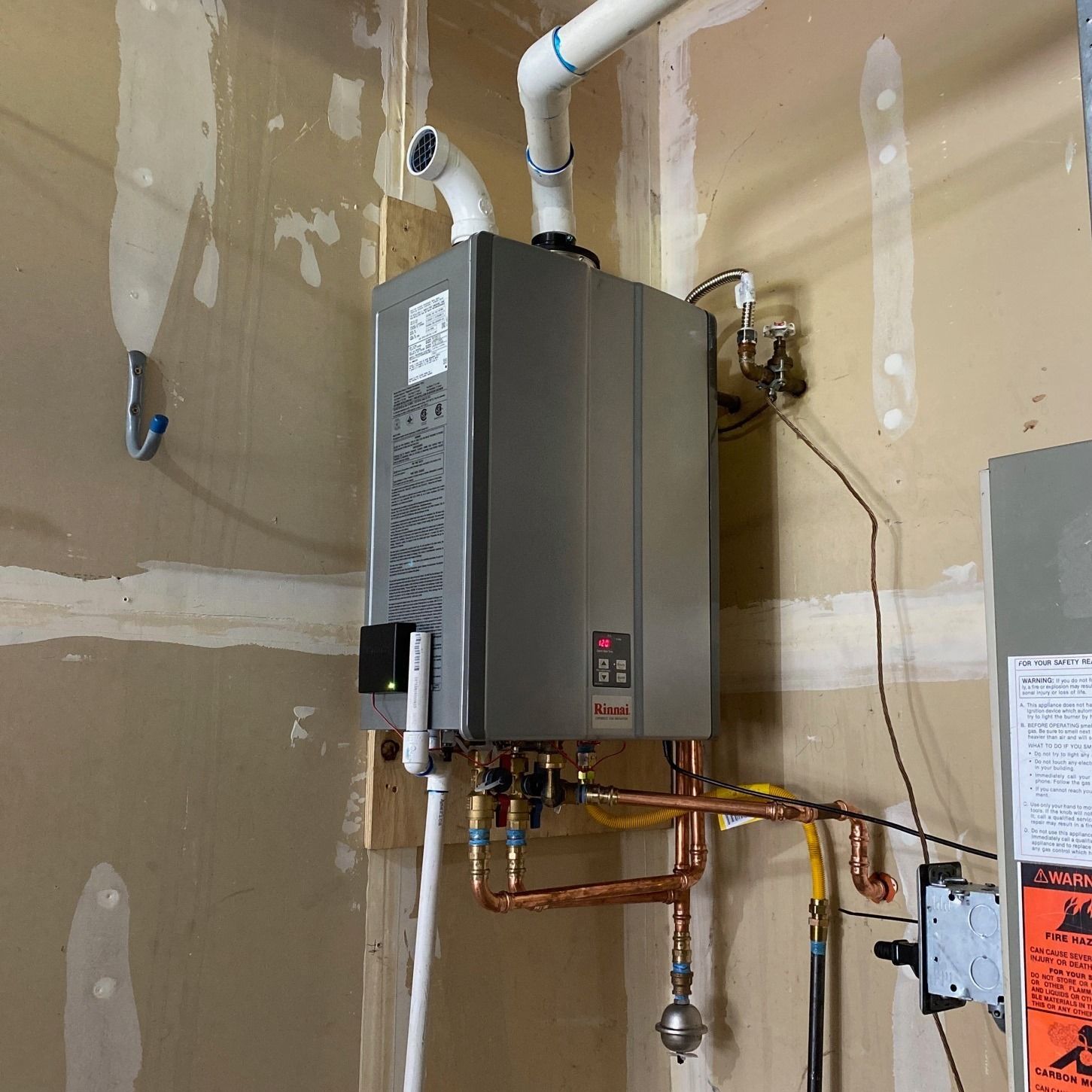 Tankless water heater installed on a wall with copper pipes and white vent pipes.
