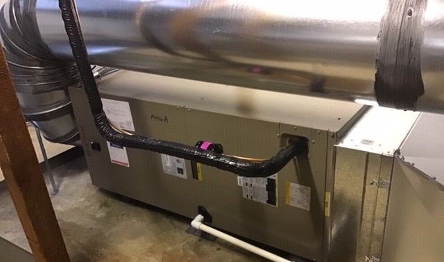 Furnace unit with ductwork and a condensate drain pipe in a basement setting.