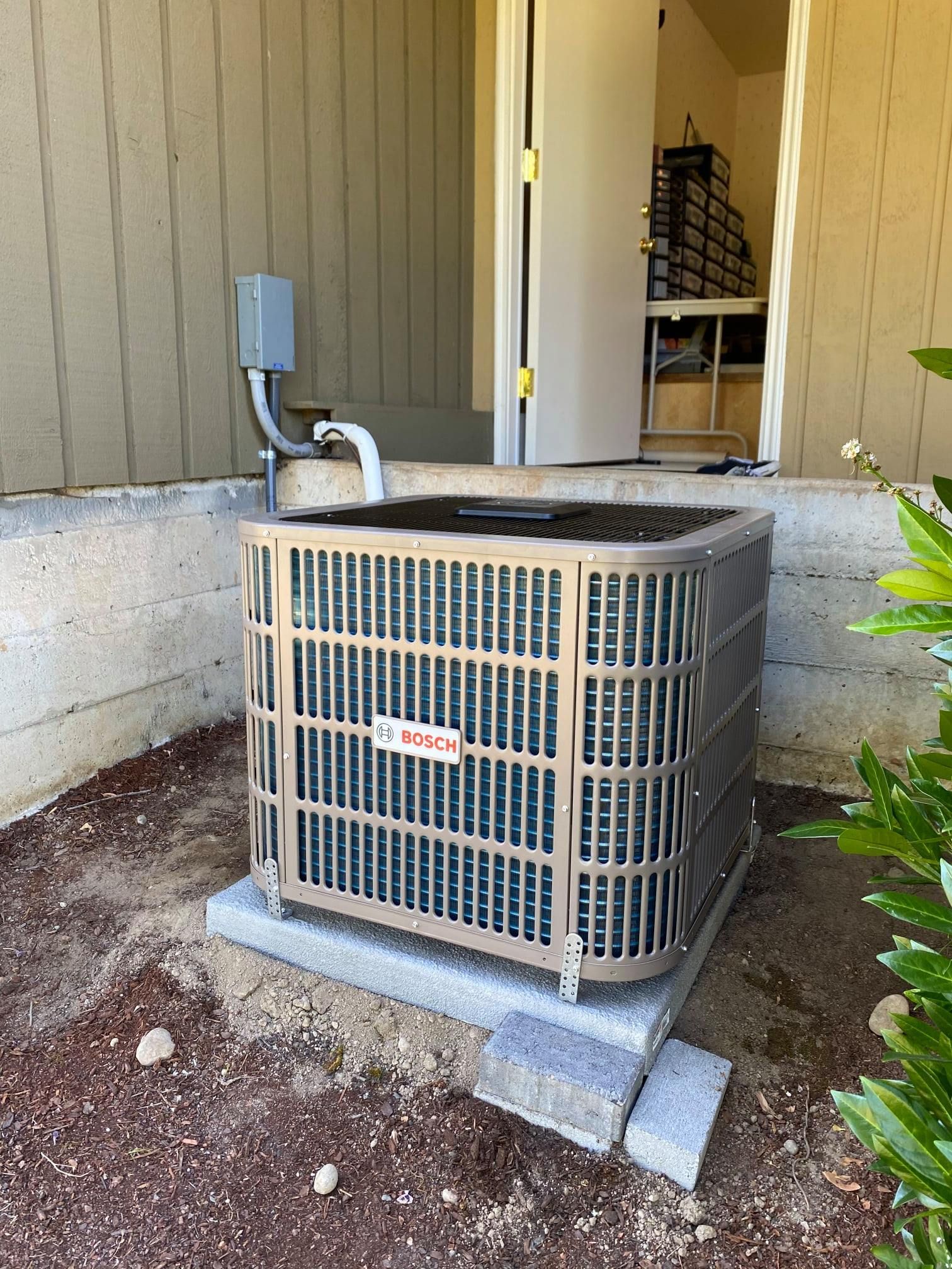 Air conditioning unit outside a building, on a concrete pad, next to a door.