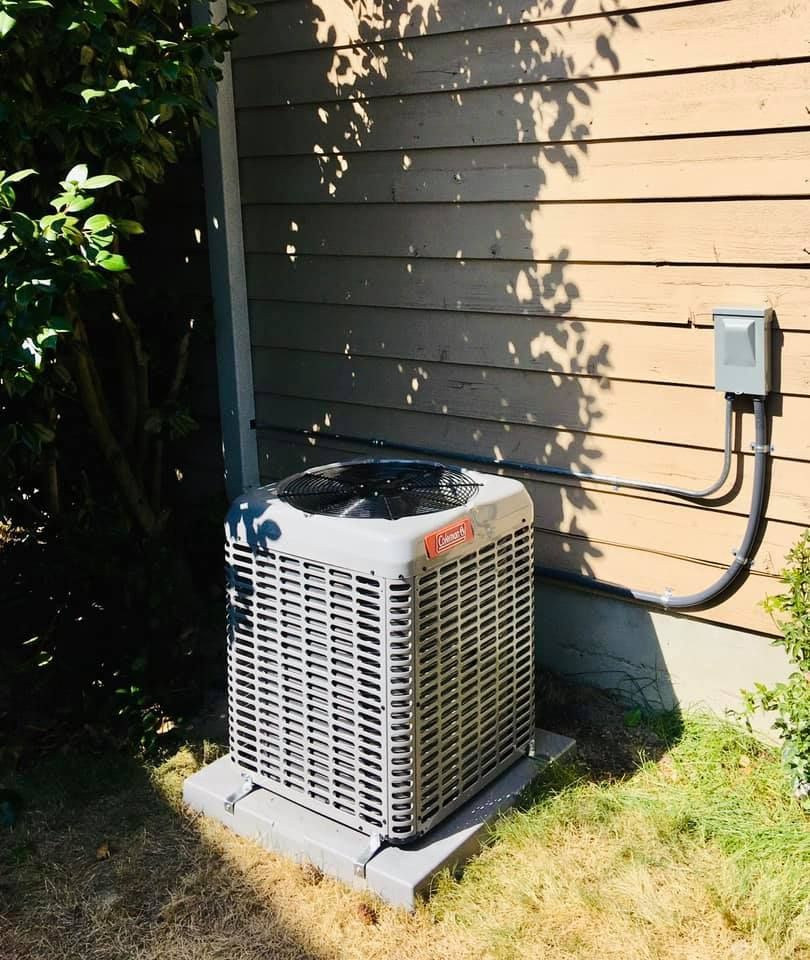 Air conditioning unit on a concrete pad next to a light brown house with a power connection.