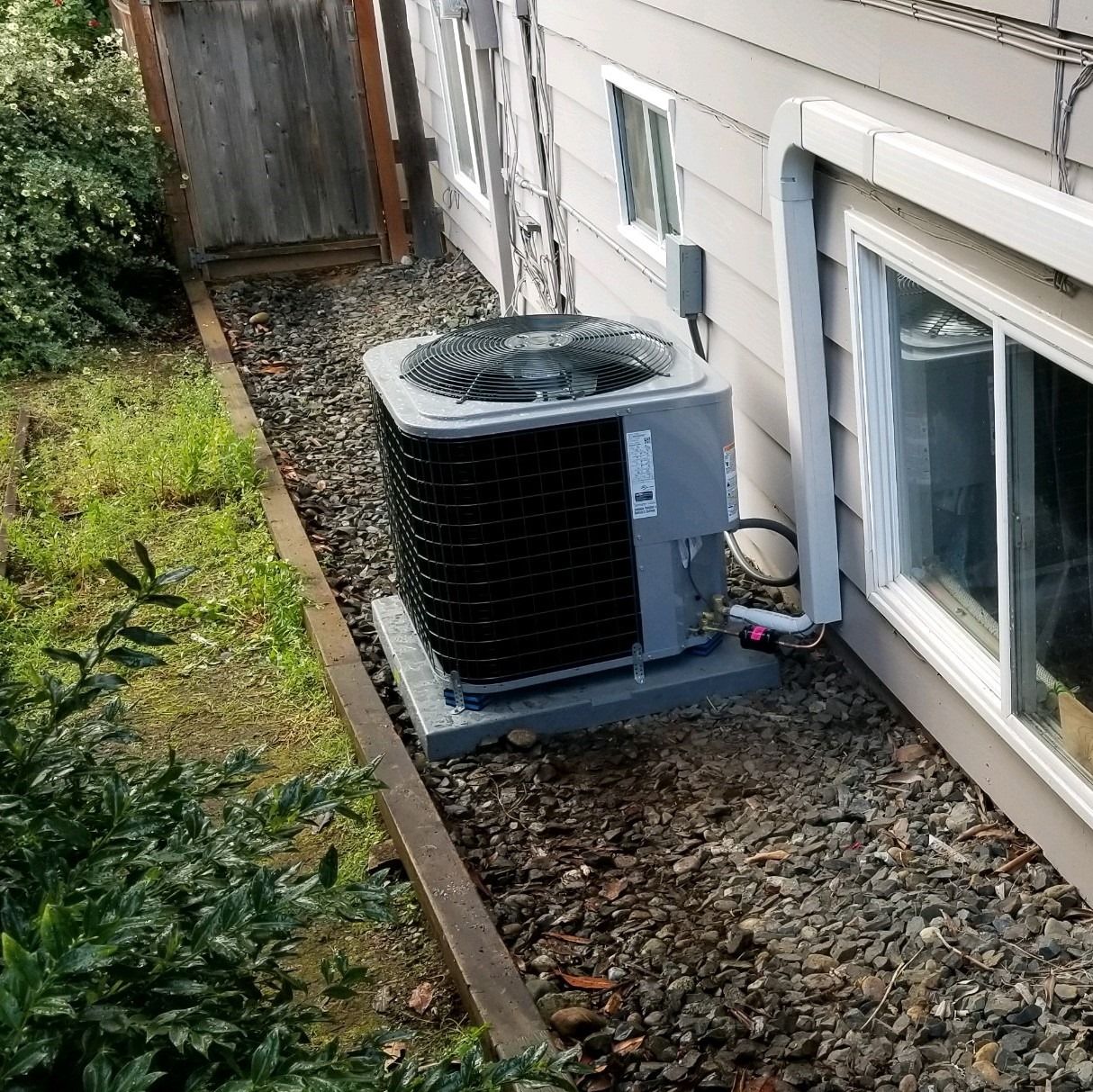 Air conditioning unit next to a house with small rocks and greenery.