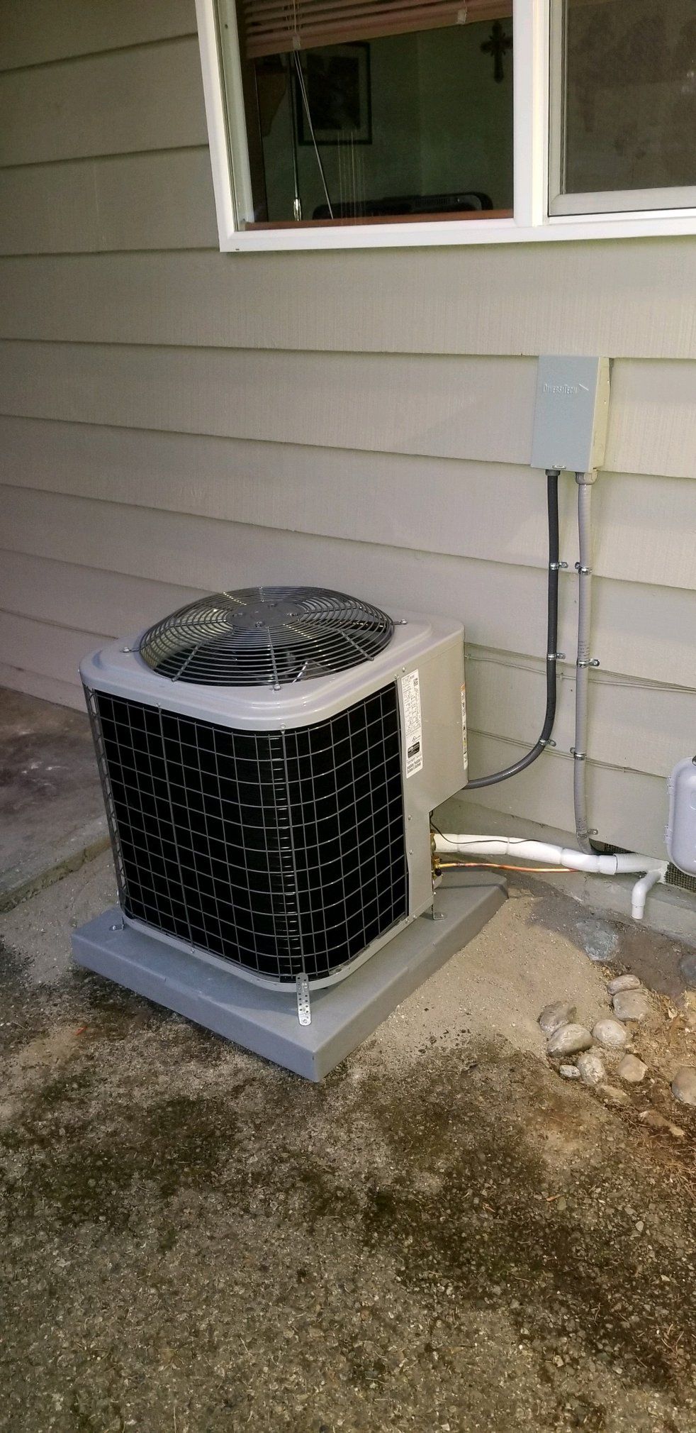 An outdoor air conditioning unit on a concrete base next to a building.