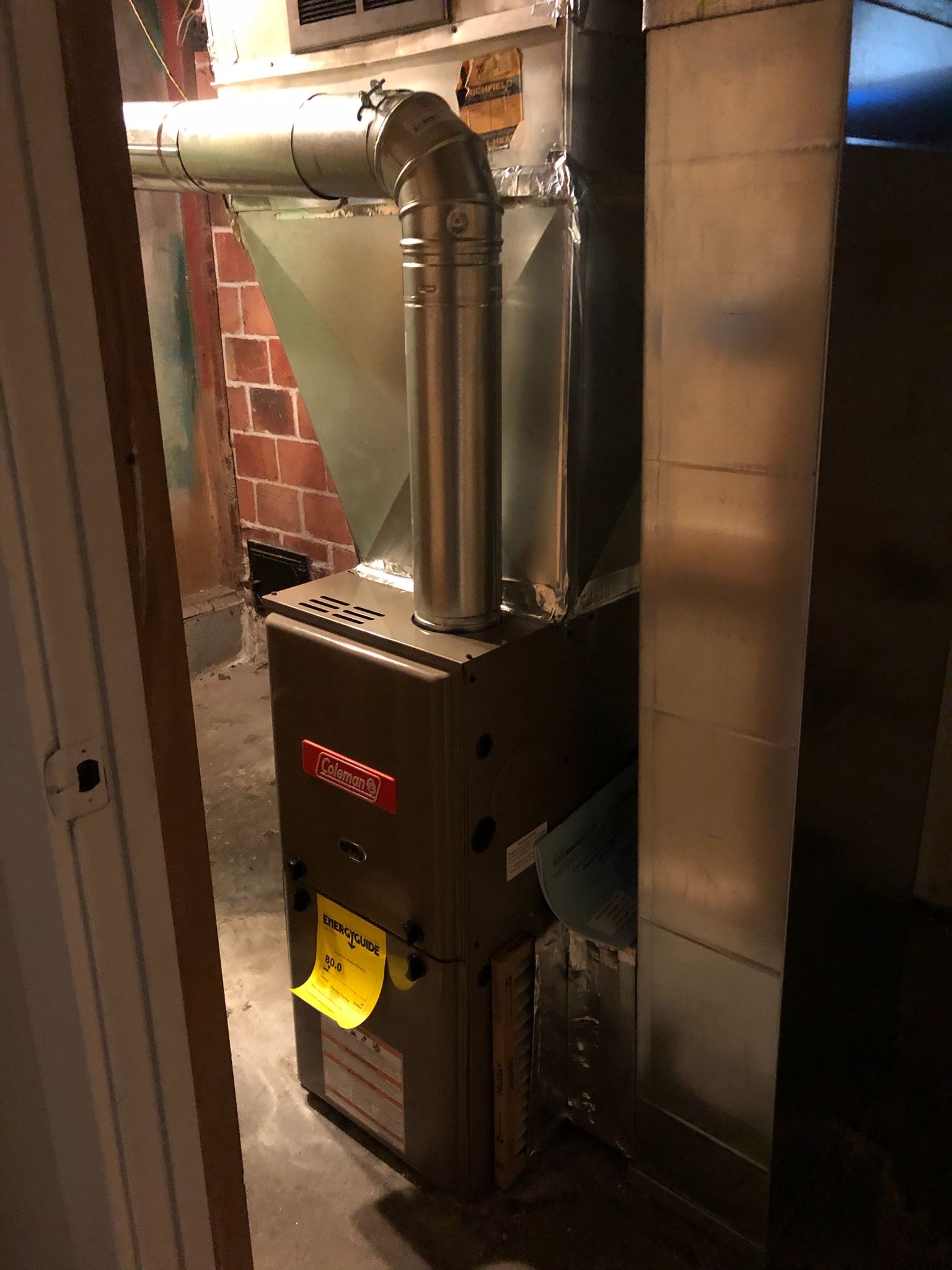 Furnace in a basement, silver metal, with flue and ductwork, brick wall background.