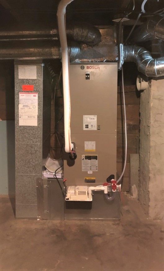 Furnace and air conditioning unit in a basement setting. The equipment is gray and connected to ductwork.