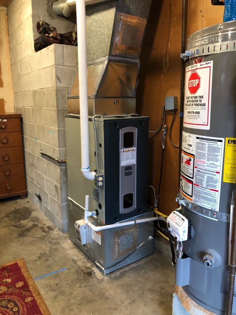 Furnace and water heater in a basement setting. The furnace is connected to ductwork and a white PVC pipe.