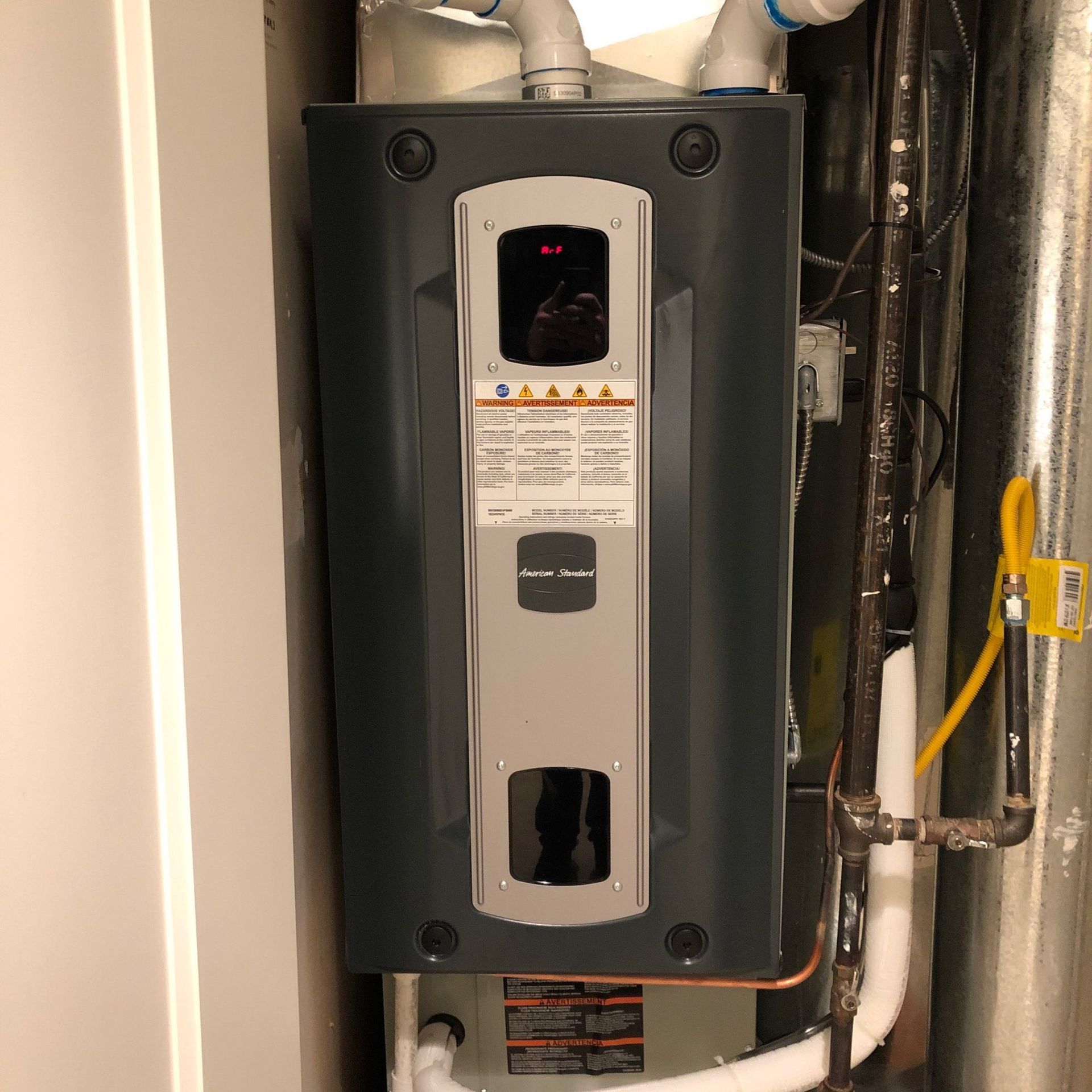 Furnace in a home, grey metal with white pipes, vents and gas line.