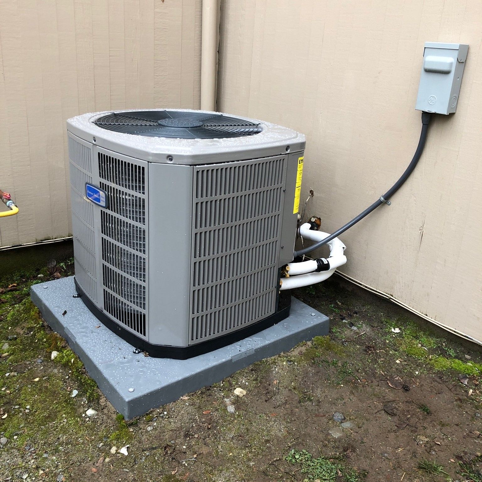 Gray air conditioning unit on a concrete pad, next to a building.