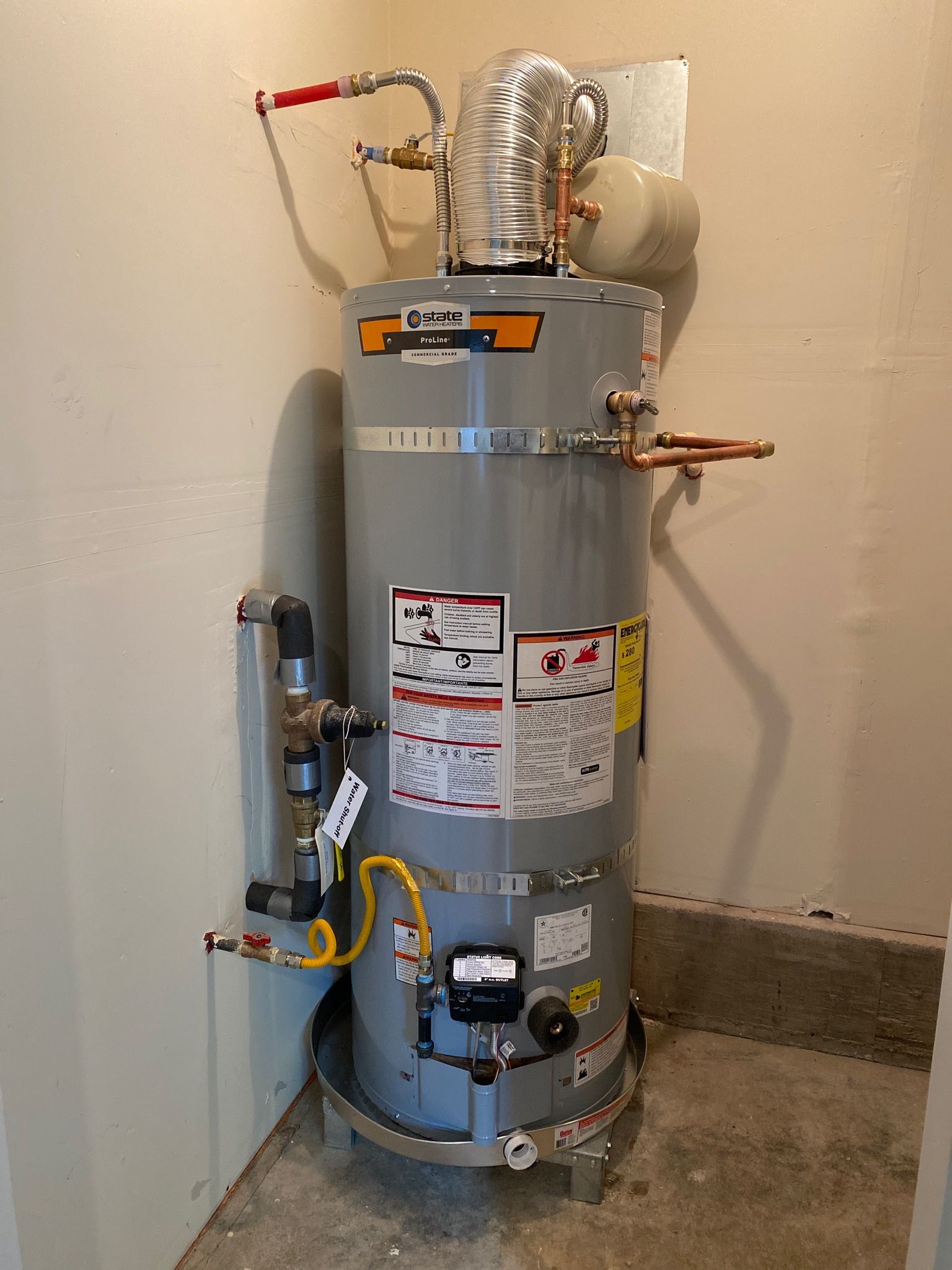 A tall, gray water heater with attached pipes and venting in a corner.