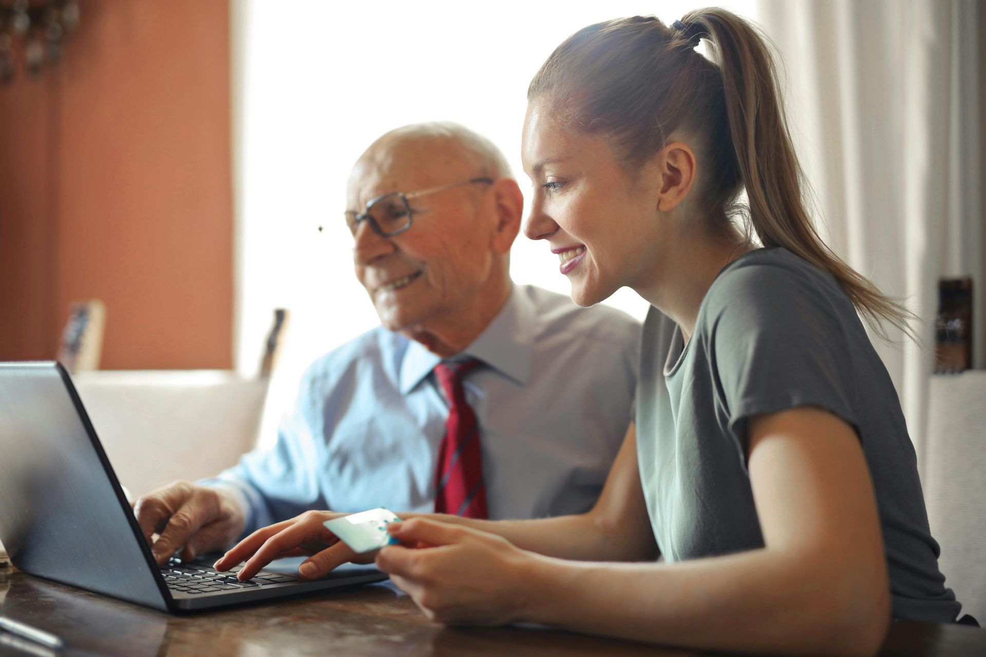 An elderly man and a young woman are sitting at a table using a laptop computer.