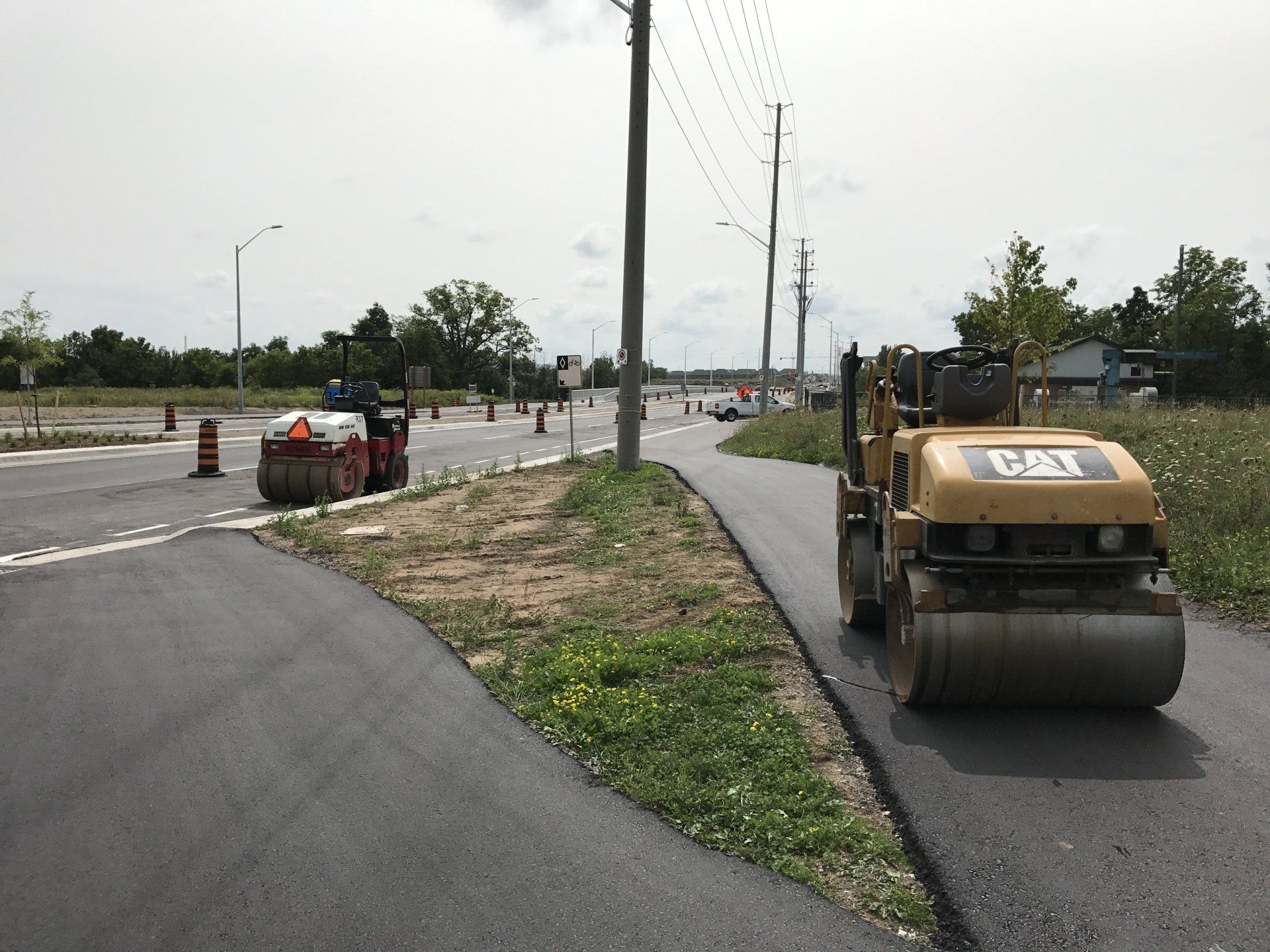 A cat roller is working on the side of a road