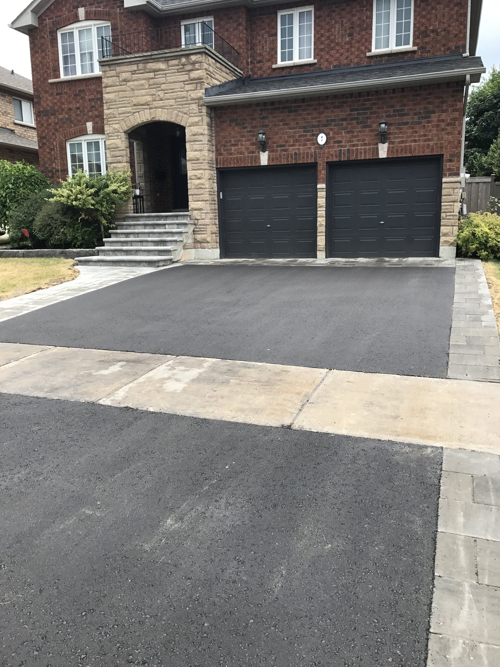 A large brick house with a black garage door and a black driveway.