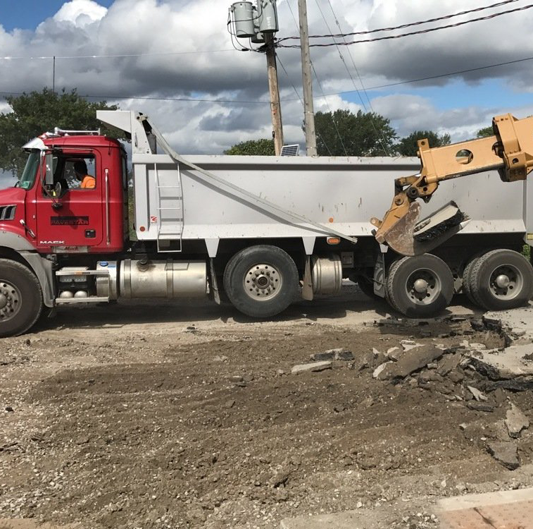 A dump truck is being loaded with dirt by a bulldozer