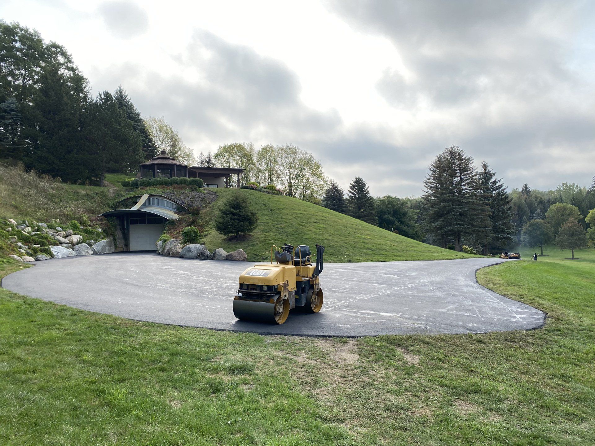 A yellow roller is rolling asphalt in a driveway.