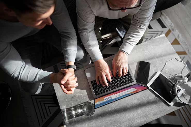 Three people leaning over a laptop on a table in a bright office setting