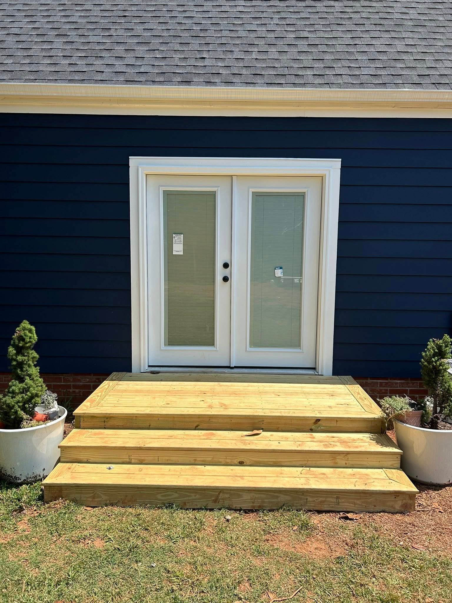 A set of wooden steps leading up to double white doors on a house with dark blue horizontal siding.